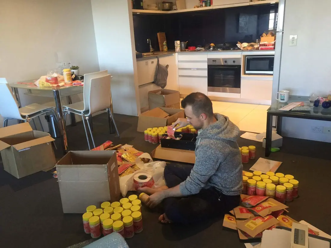 Mike sitting on a kitchen floor surrounded by boxes and tubs, packing orders