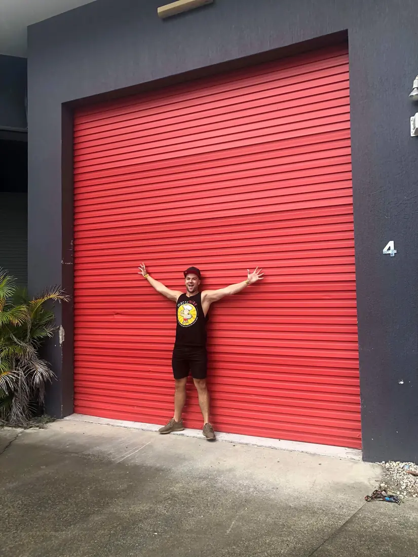 Mike with arms spread in front of a red warehouse roller door